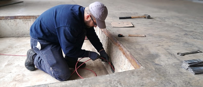Operario instalando cableado en el foso de una rampa niveladora a medida para su modernización